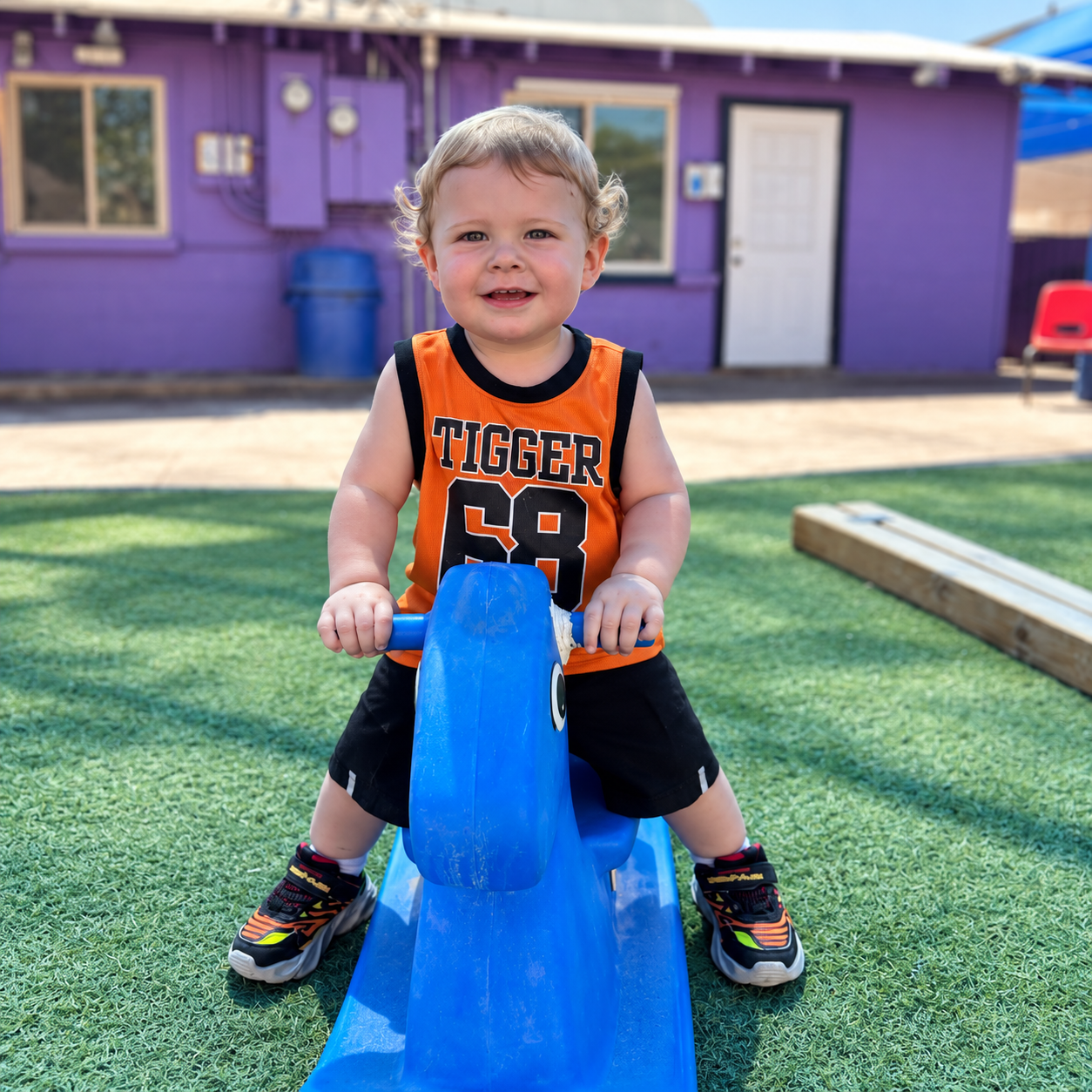 A smiling toddler riding a blue playground toy at Kidz-Zona