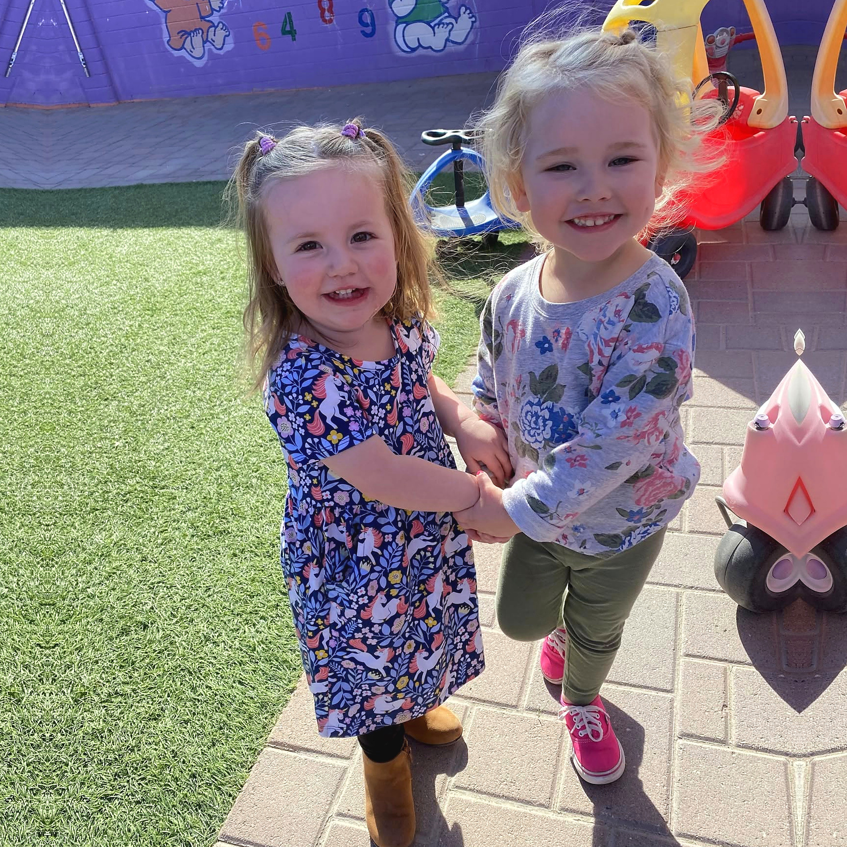 Two smiling preschool girls holding hands on the playground at Kidz-Zona