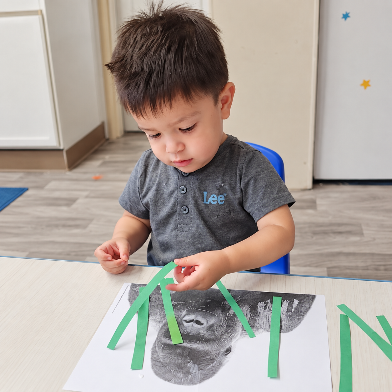 A toddler placing green paper strips onto an animal craft at a Kidz-Zona classroom table