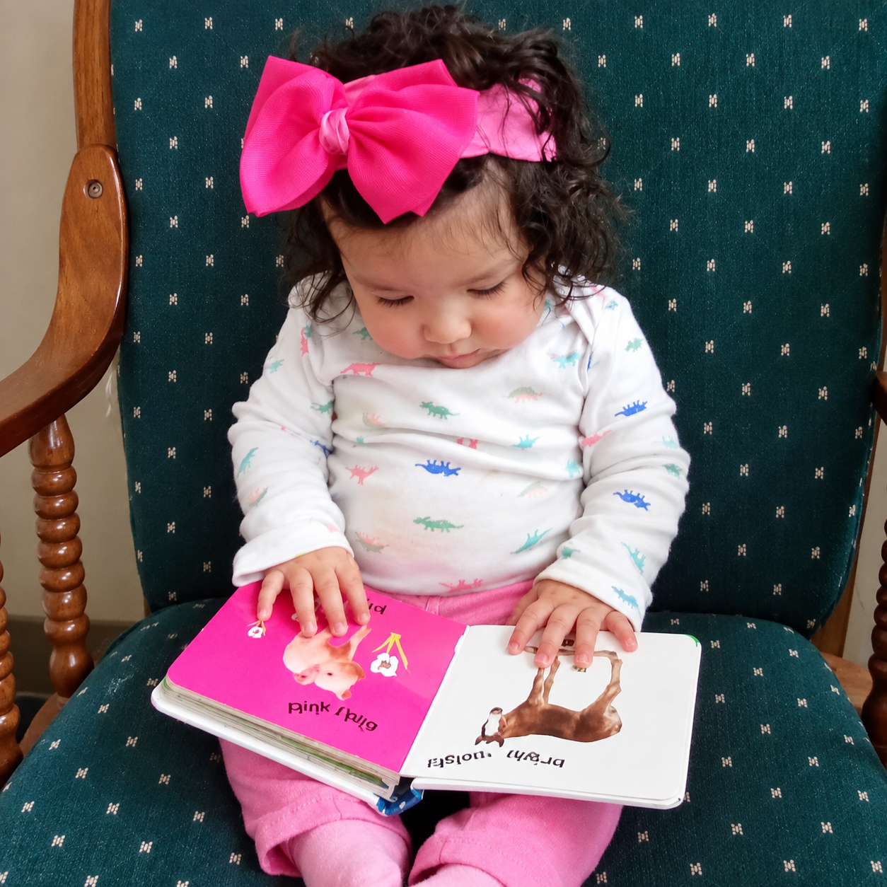 An infant sitting in a chair looking at a picture book at Kidz-Zona